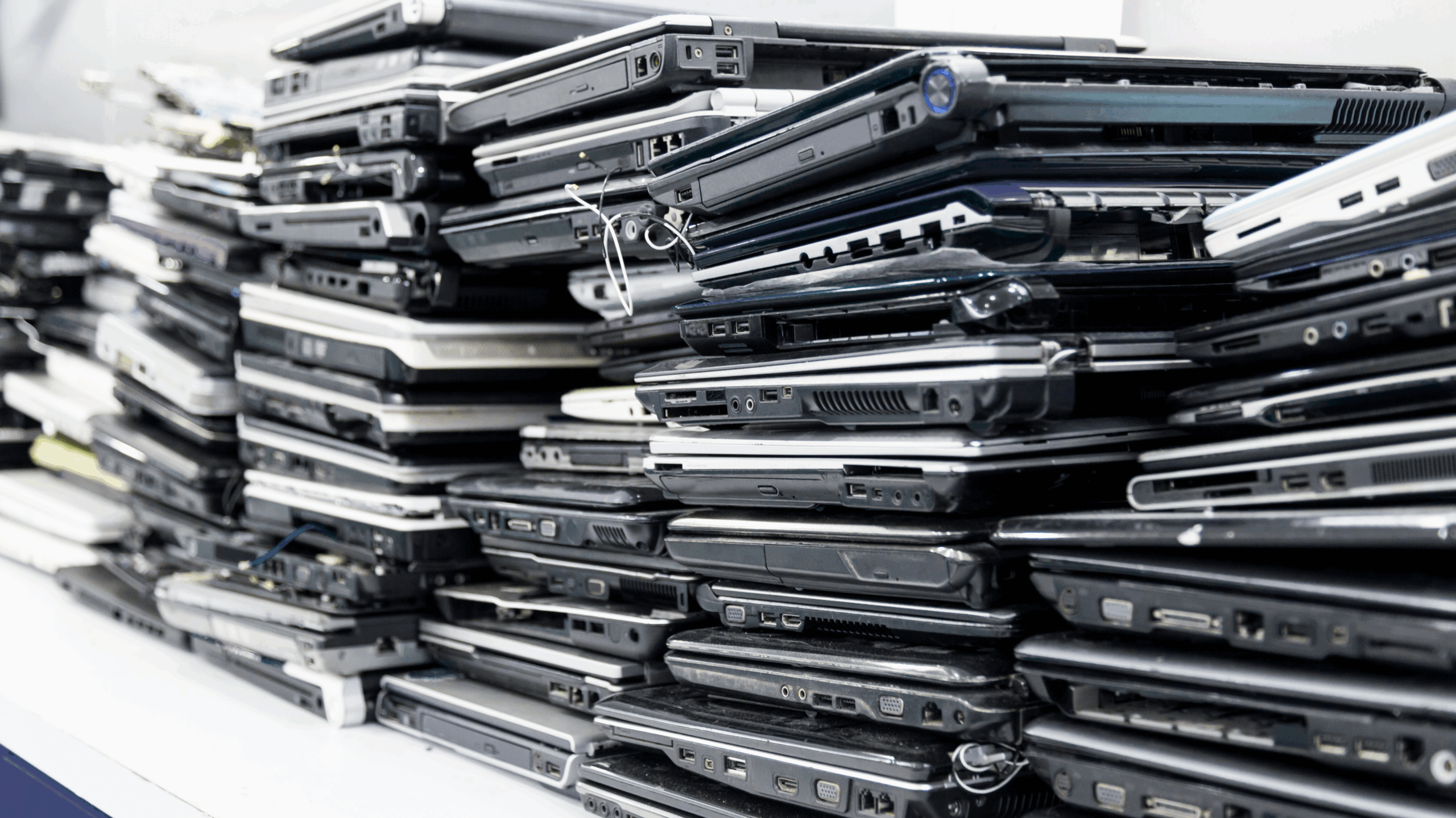 A pile of broken laptops stacked on a counter, illustrating the backlog and hidden costs of device downtime in schools.