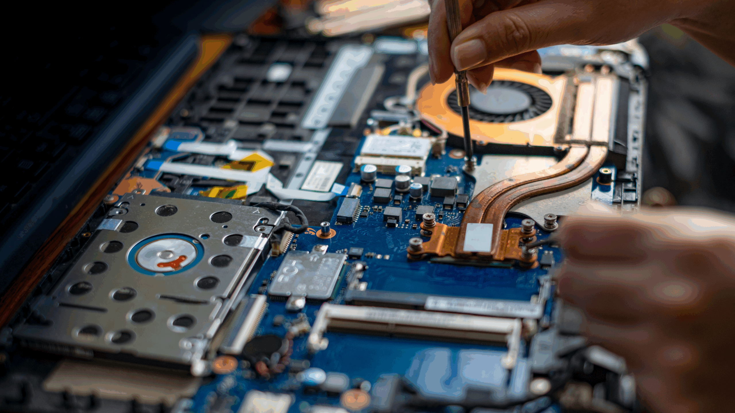 Close-up of hands repairing a laptop motherboard with screwdriver, illustrating self-service device repairs in schools.