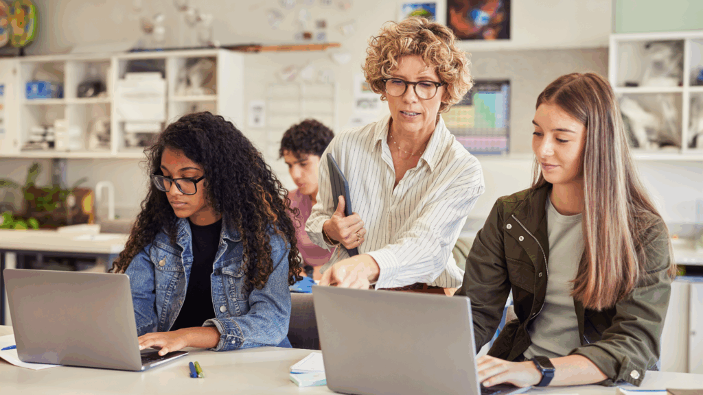 Teacher overseeing students working on laptops, representing the importance of oversight and AI policy in K–12 districts for safety